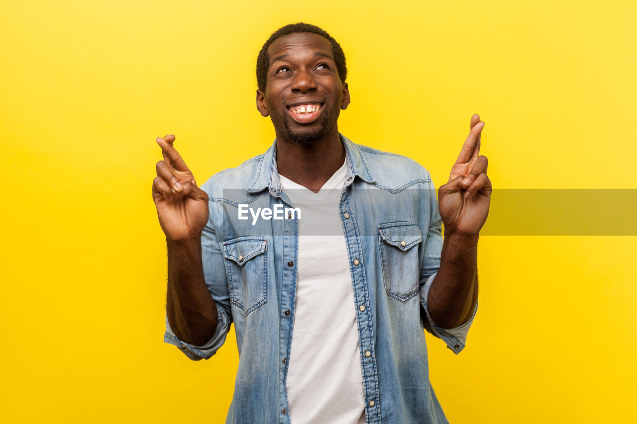 Portrait of young man standing against yellow background