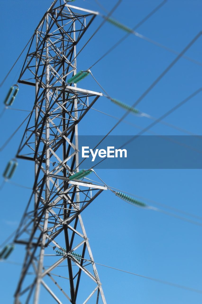 Low angle view of electricity tower against clear blue sky