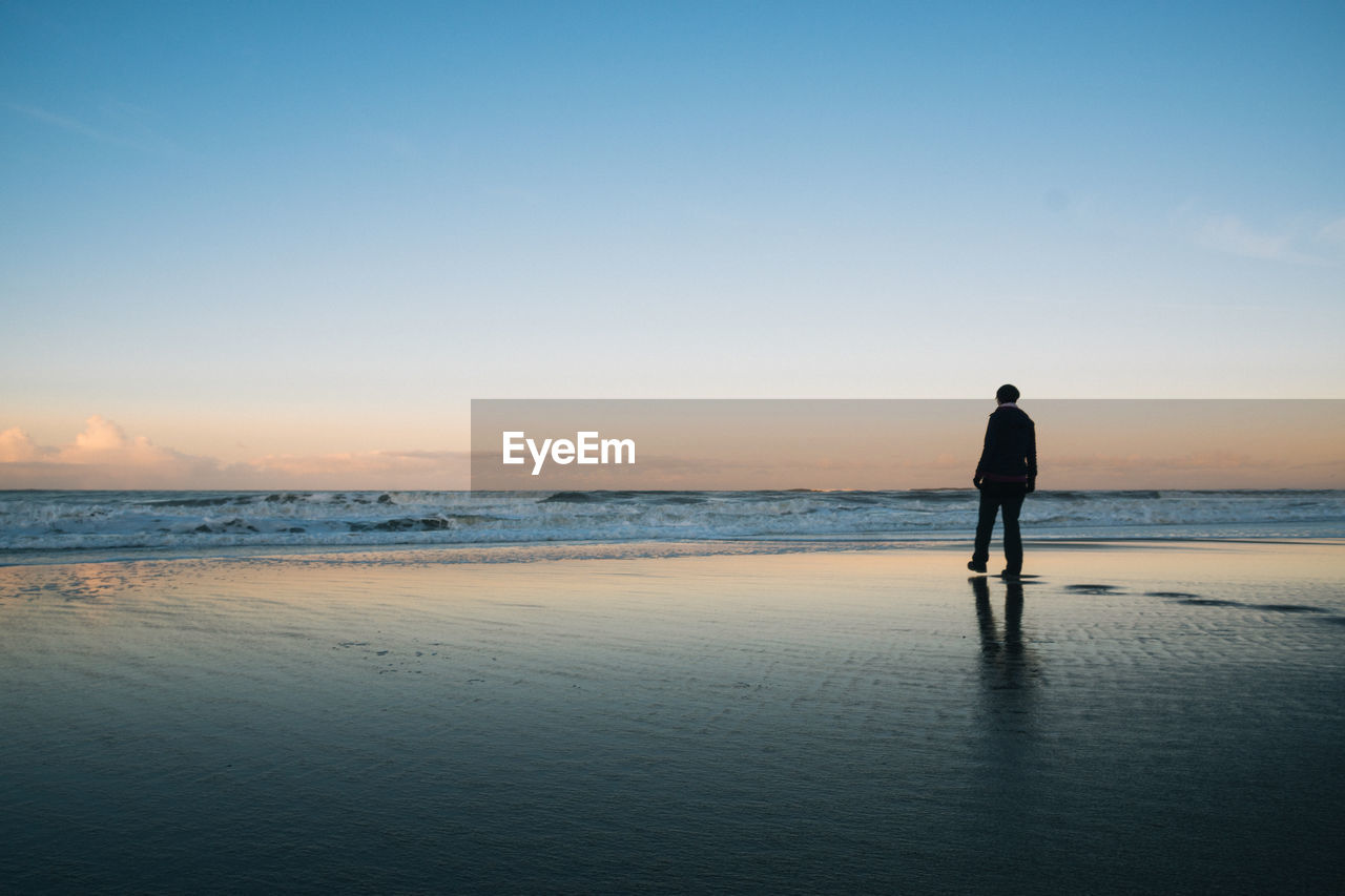 Rear view of man standing on beach during sunset