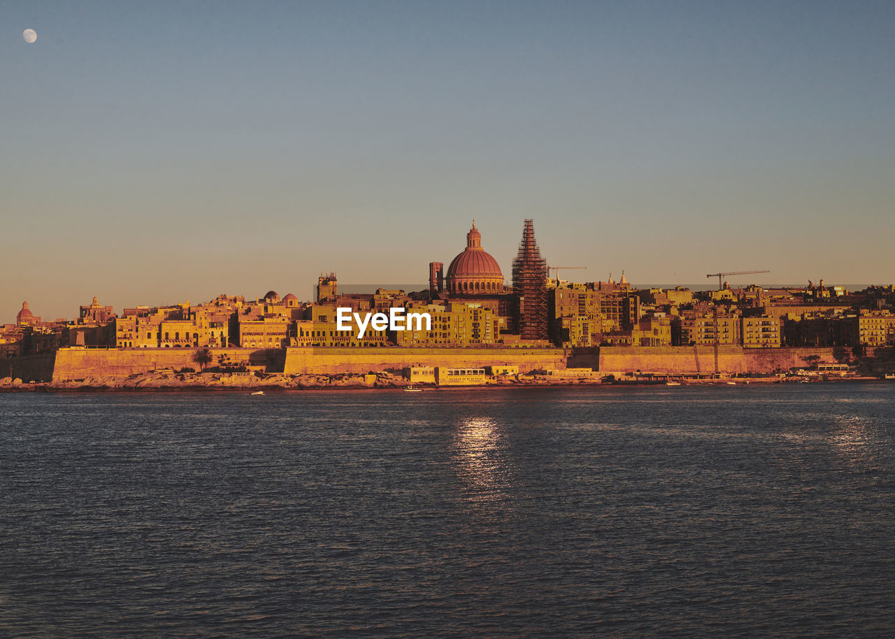 Buildings of valetta by sea against sky during sunset