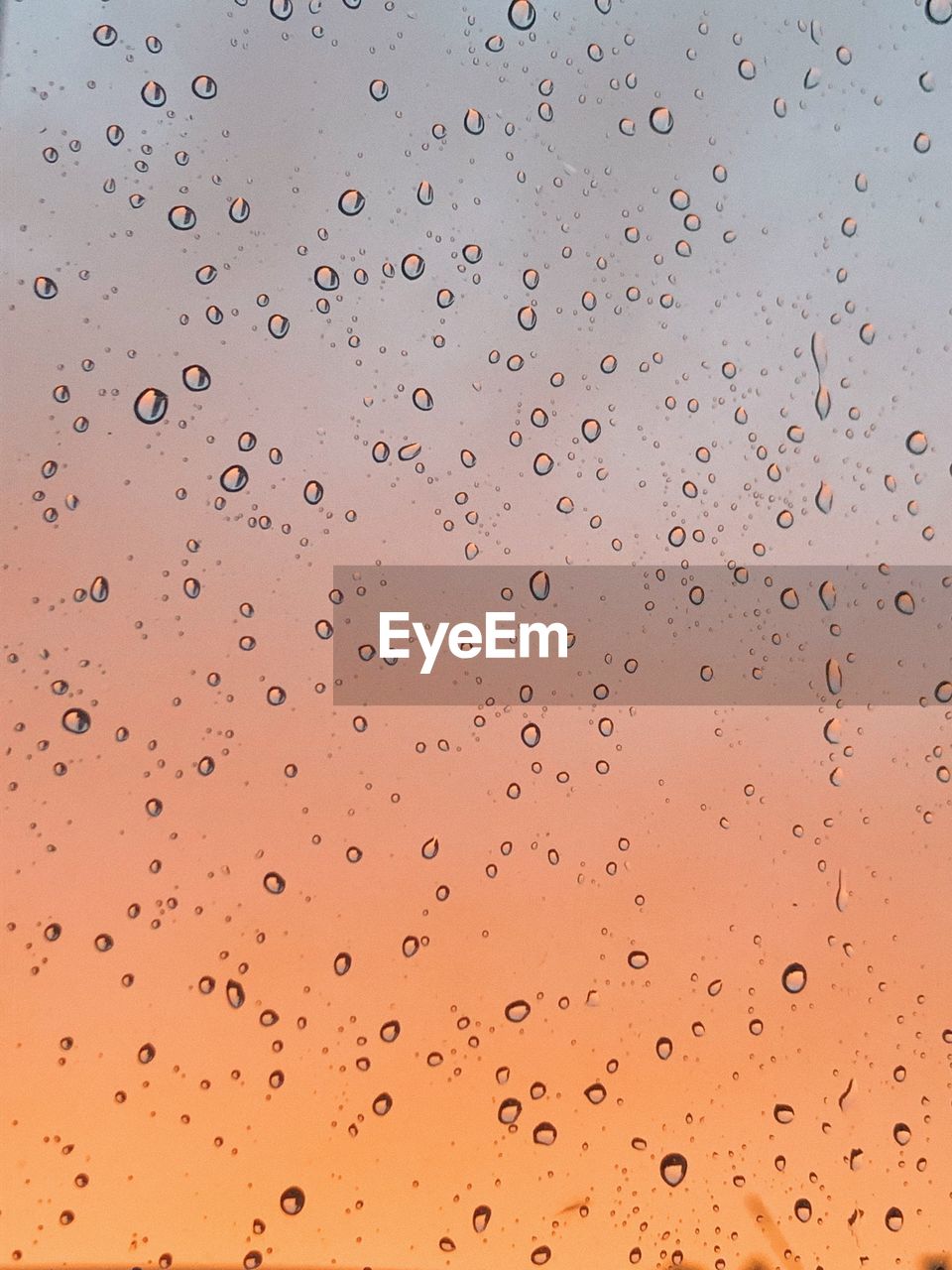 View of rain drops on a window against the sky during colourful sunset
