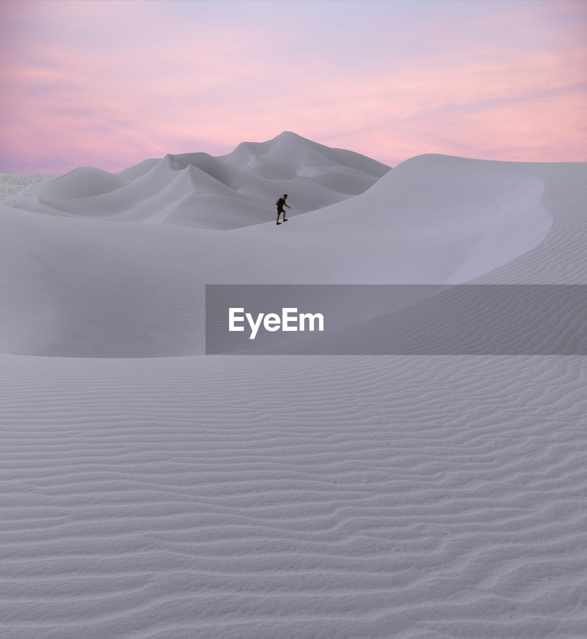 Man walking on desert against sky during sunset