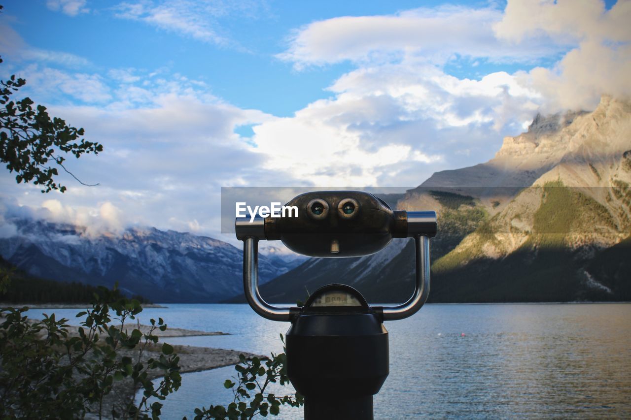 CLOSE-UP OF COIN-OPERATED BINOCULARS BY LAKE AGAINST MOUNTAIN RANGE