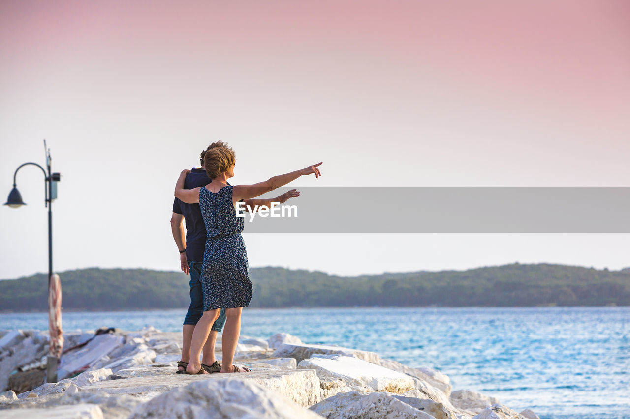 Full length of couple standing on pier by sea against clear sky