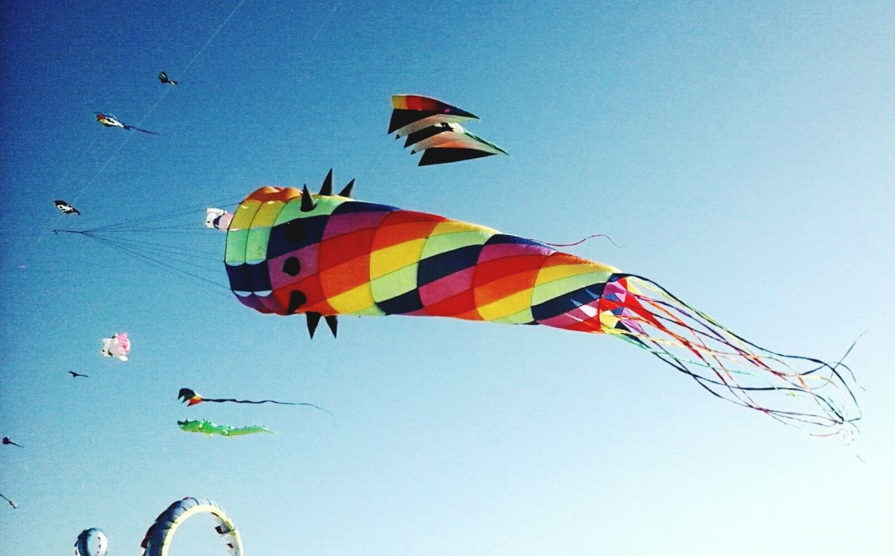 Low angle view of kites flying against clear blue sky on sunny day