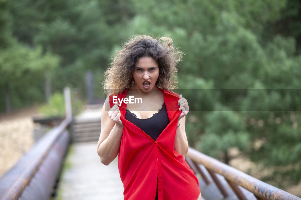 women, adult, one person, red, hairstyle, clothing, dress, young adult, photo shoot, smiling, portrait, lifestyles, curly hair, emotion, happiness, fashion, nature, tree, front view, brown hair, person, long hair, leisure activity, looking at camera, female, outdoors, cheerful, day, portrait photography, positive emotion, plant, forest, exercising, vitality, enjoyment, waist up, relaxation, human face