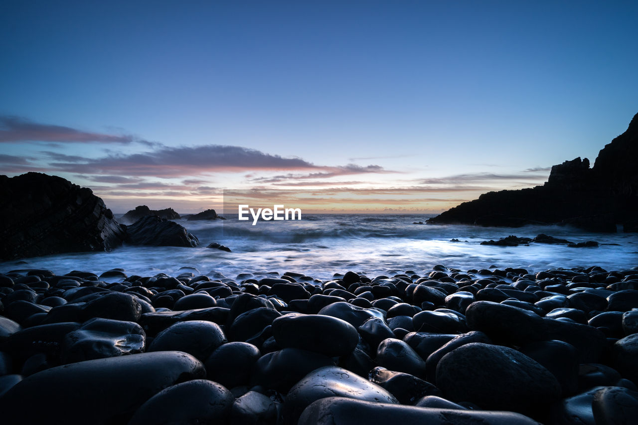 Rocks on beach against sky during sunset