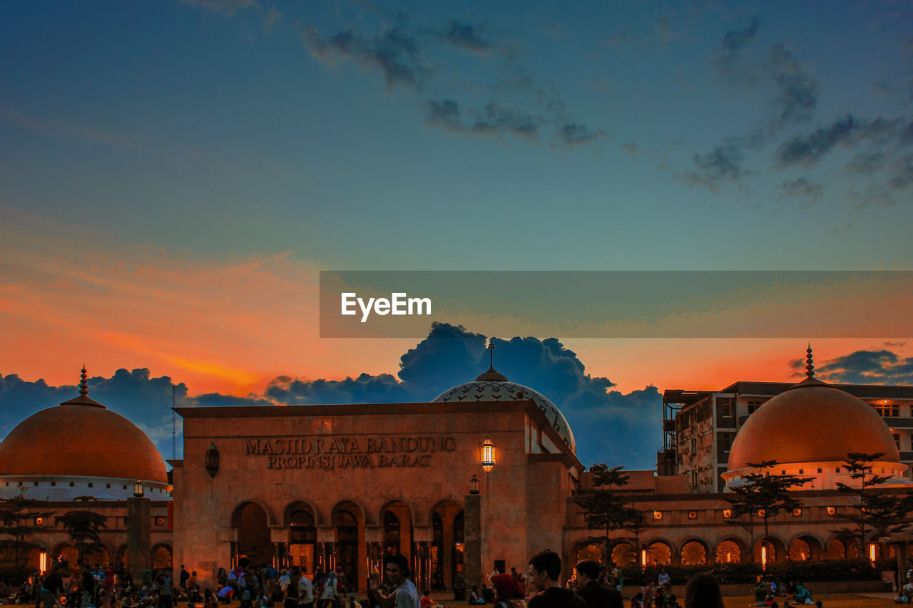 GROUP OF PEOPLE IN FRONT OF TEMPLE AGAINST SKY DURING SUNSET