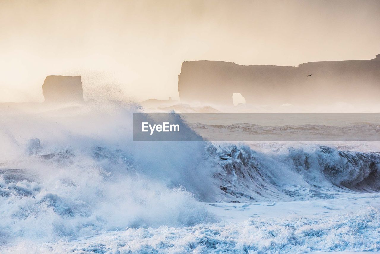 Sea waves splashing on shore against sky