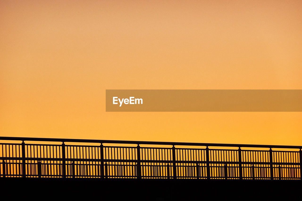 Silhouette bridge railing against sky during sunset