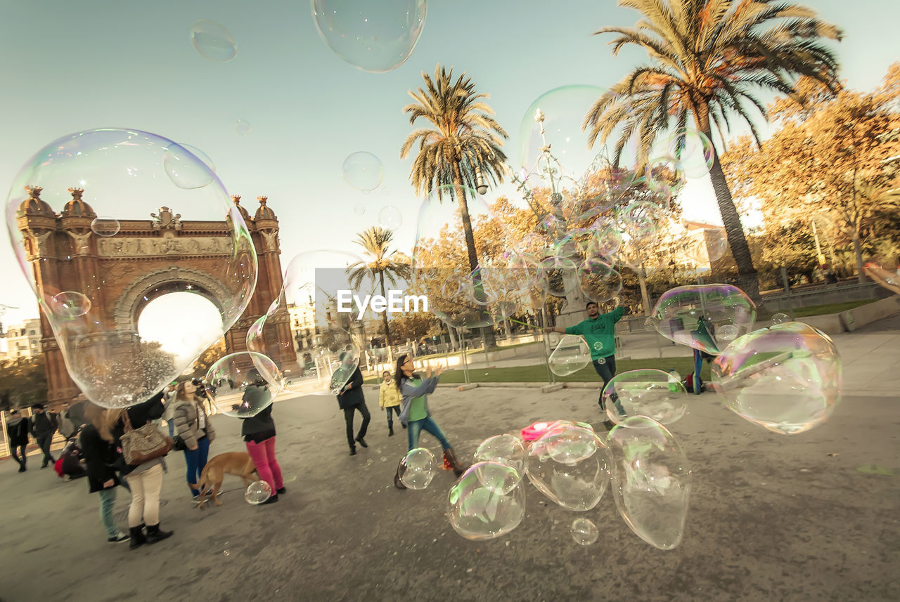Tilt image of people playing with soap bubbles at arc de triomf against sky