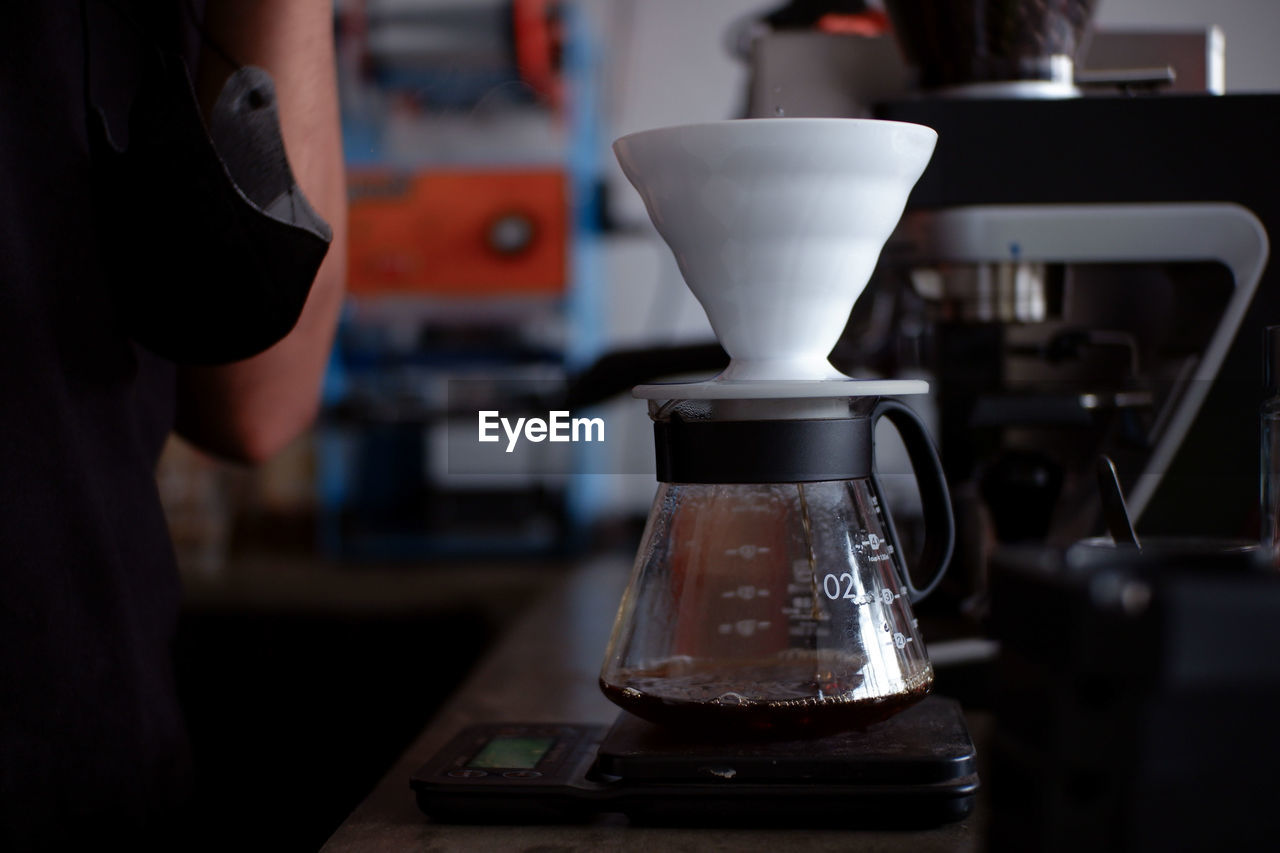 Barista pouring boiling water from a kettle into a drip coffee maker using v60 method