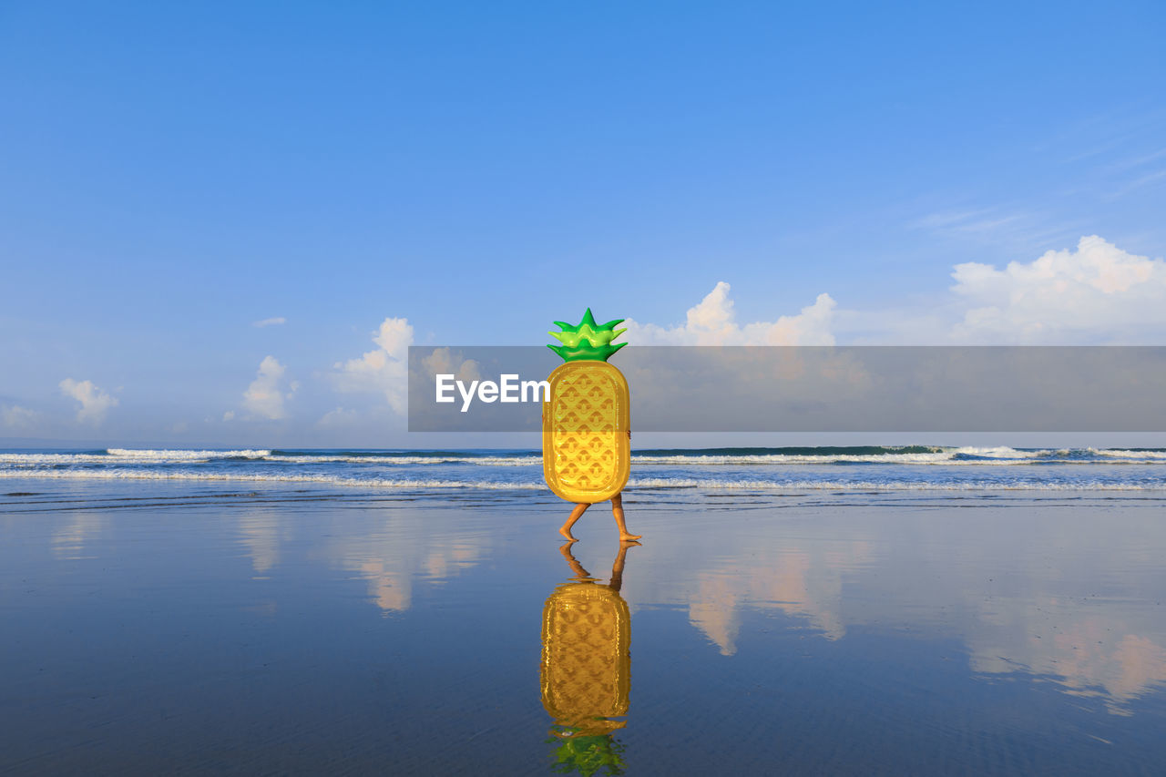 Woman with pineapple float walking at beach