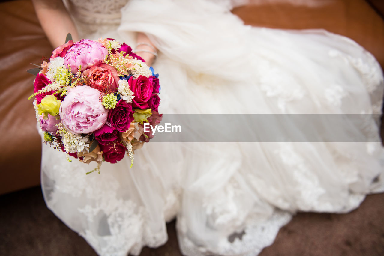 Low section of bride wearing wedding dress with bouquet
