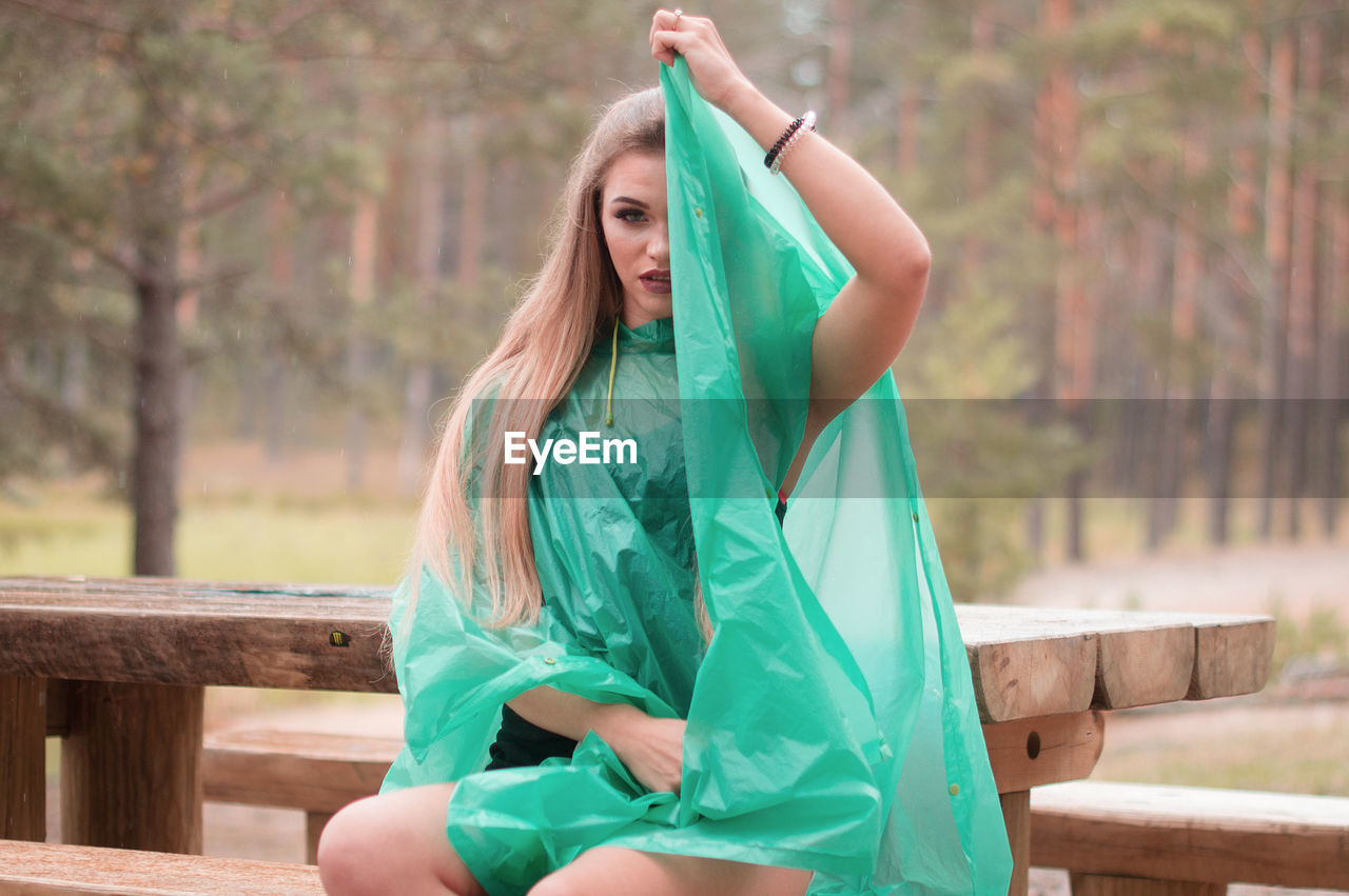 Portrait of young woman wearing raincoat sitting on seat