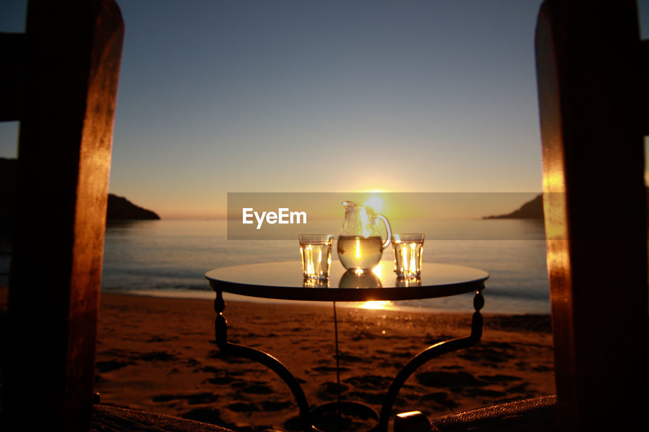 Drinking glasses and jug on table at beach during sunset