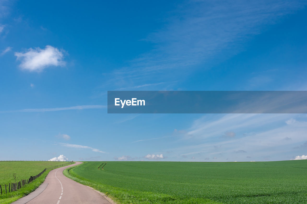 Empty road amidst field against sky