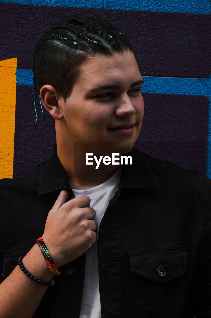 Close-up of smiling young man looking away against wall