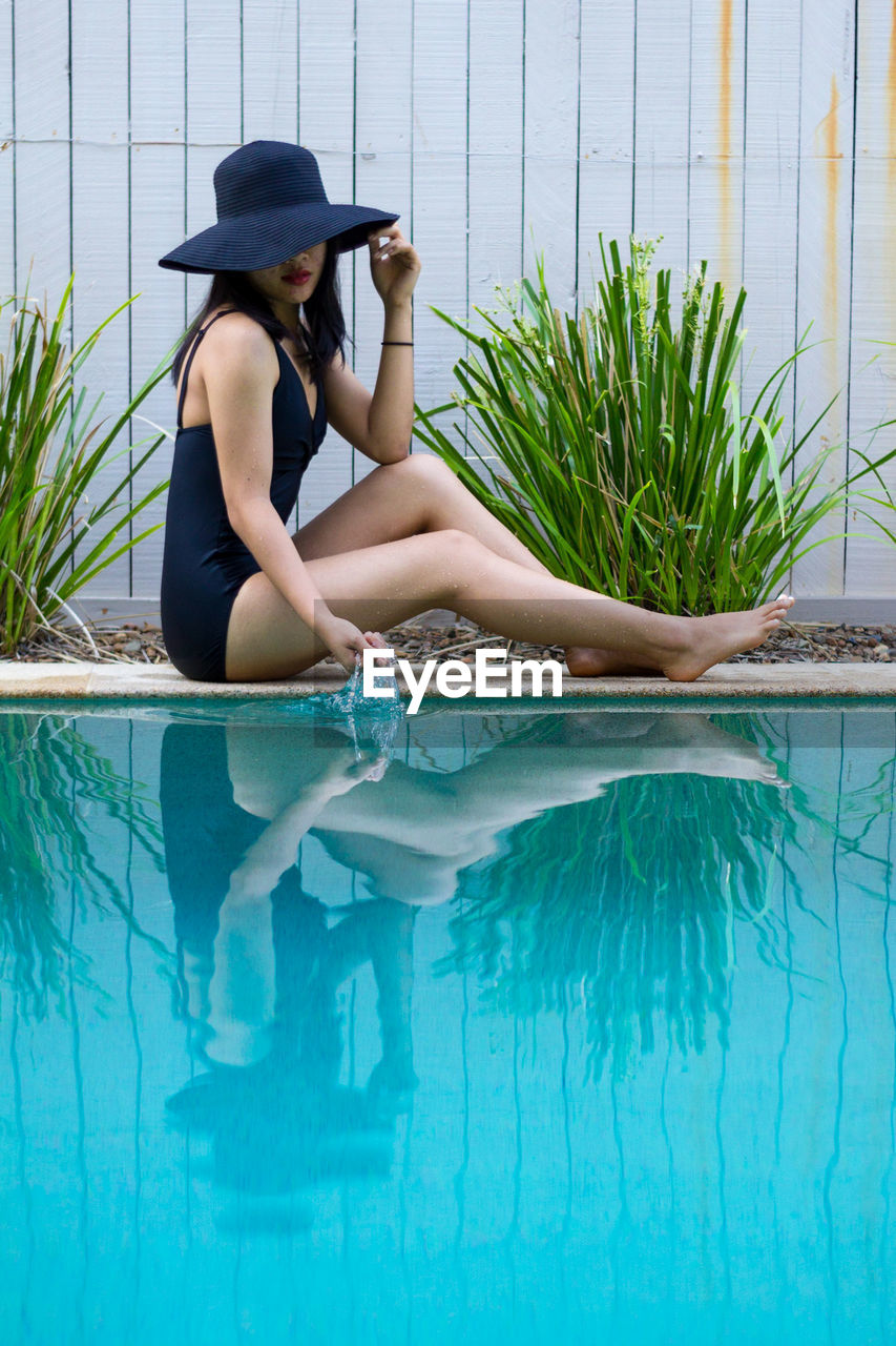 Asian woman wearing a black hat and swimsuit while touching the water