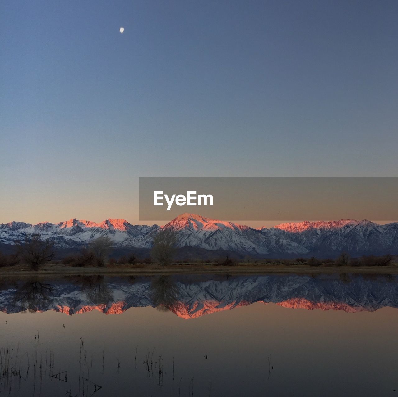 Idyllic shot of snowcapped mountains reflection in lake against clear sky during sunrise