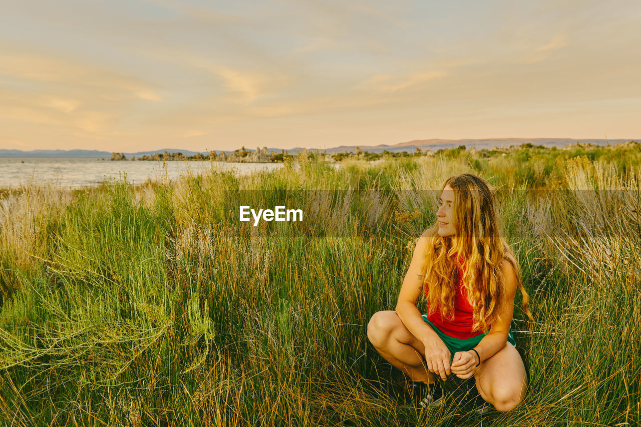 Young woman sitting in tall grass by mono lake in northern california.