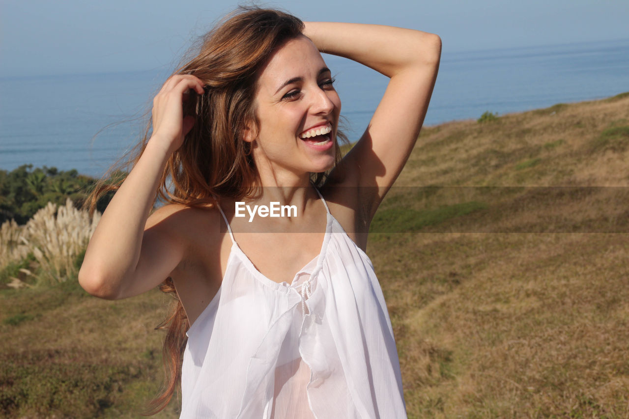 Portrait of a happy young woman smiling in a field with the sea in the background.