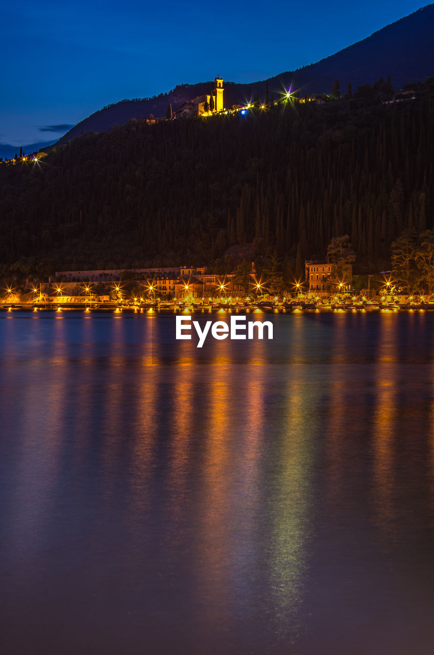 ILLUMINATED BUILDINGS BY LAKE AGAINST SKY AT DUSK