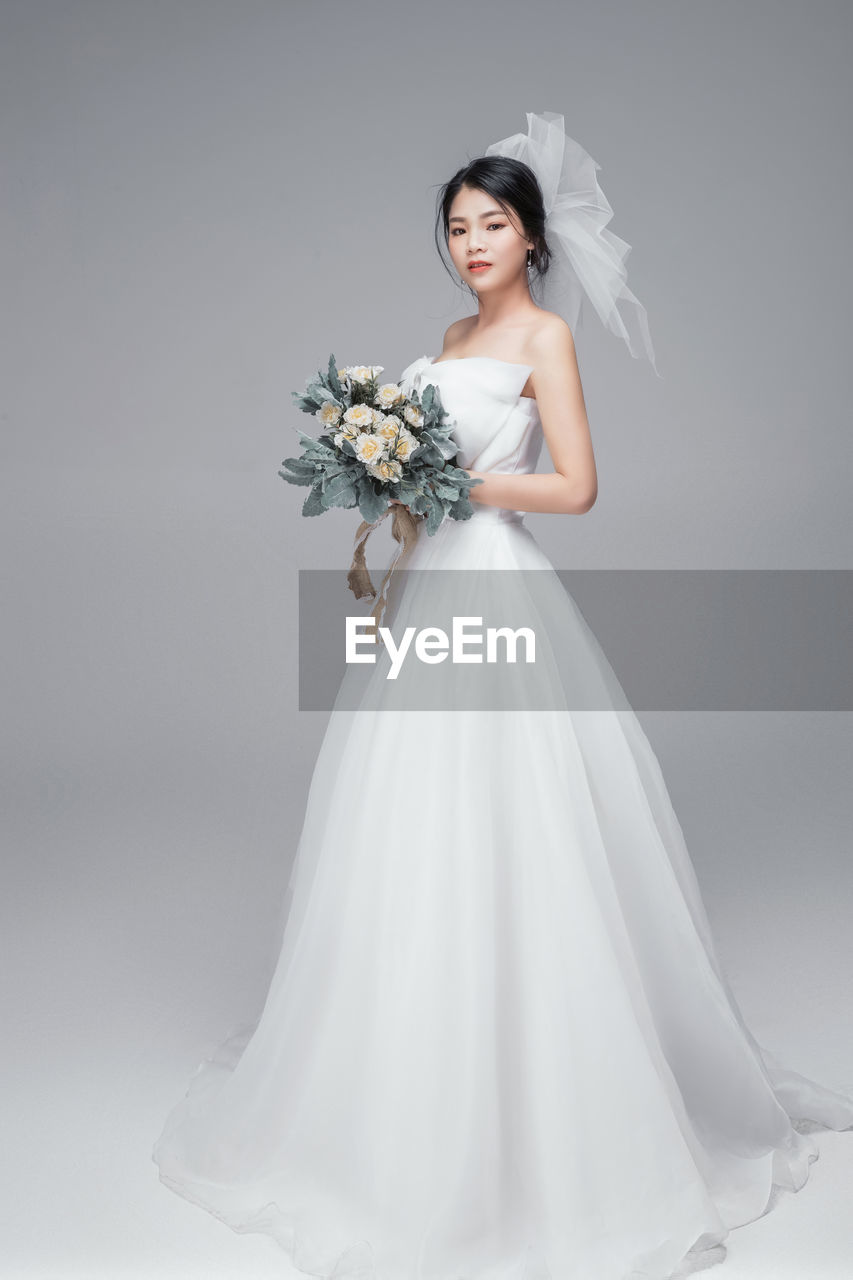 Portrait of bride with bouquet standing against gray background