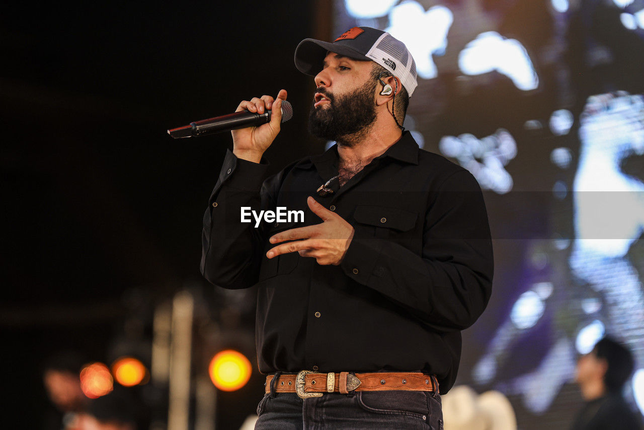performance, adult, musician, men, music, concert, singing, beard, night, person, arts culture and entertainment, facial hair, stage, one person, clothing, hat, standing, young adult, waist up, performing arts, entertainment, microphone, holding, city, occupation, input device, nightlife, illuminated