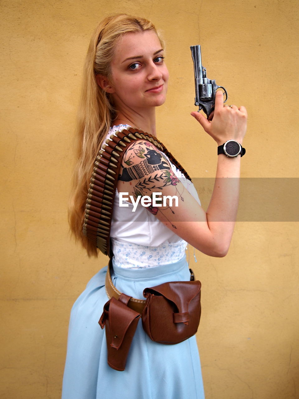 Portrait of beautiful woman holding gun while standing against wall