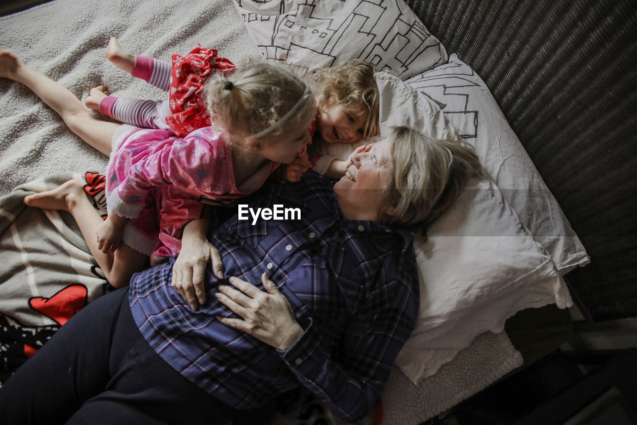 Overhead view of happy granddaughters with grandmother on bed