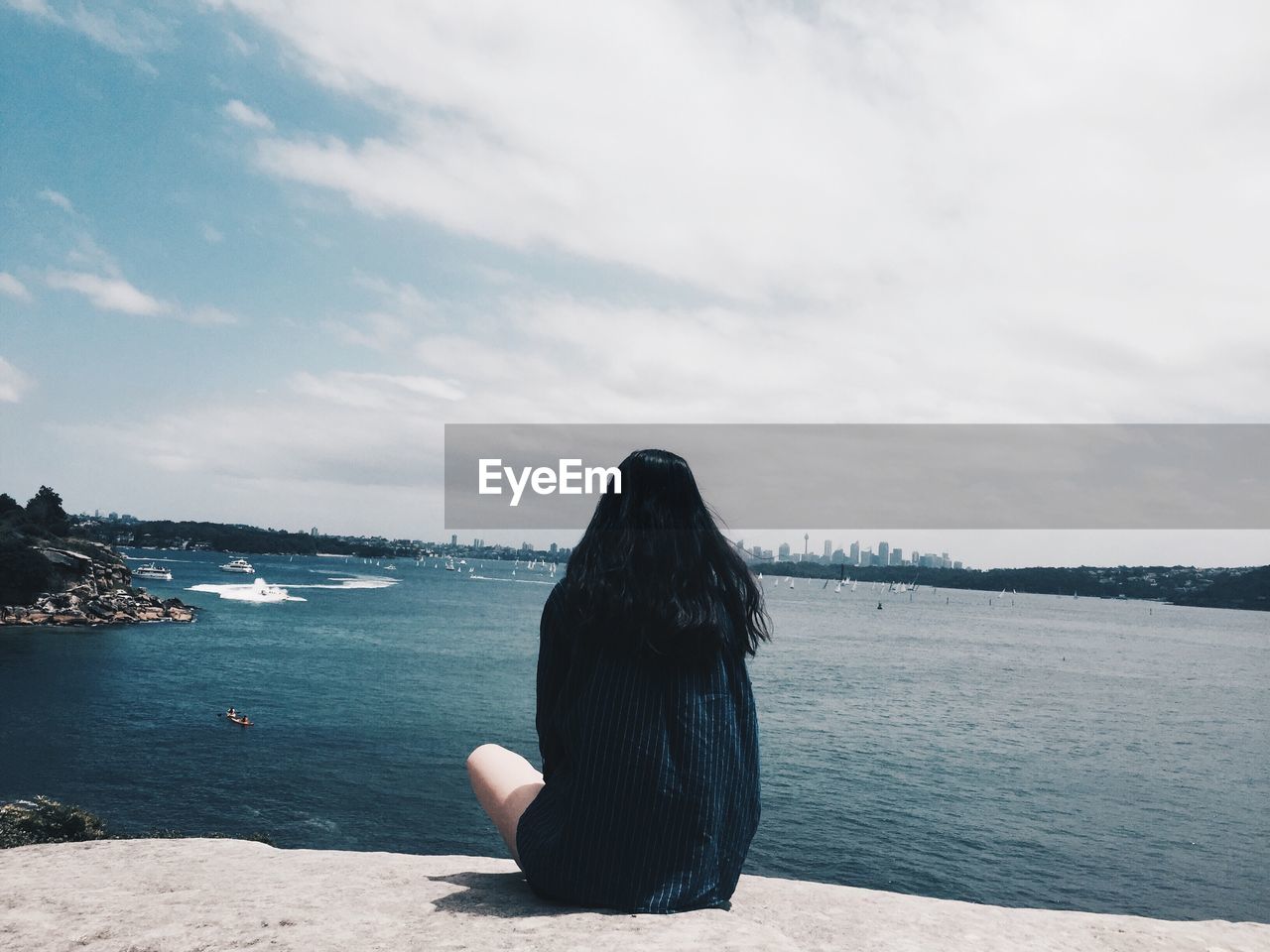 Rear view of woman sitting on rock against sea