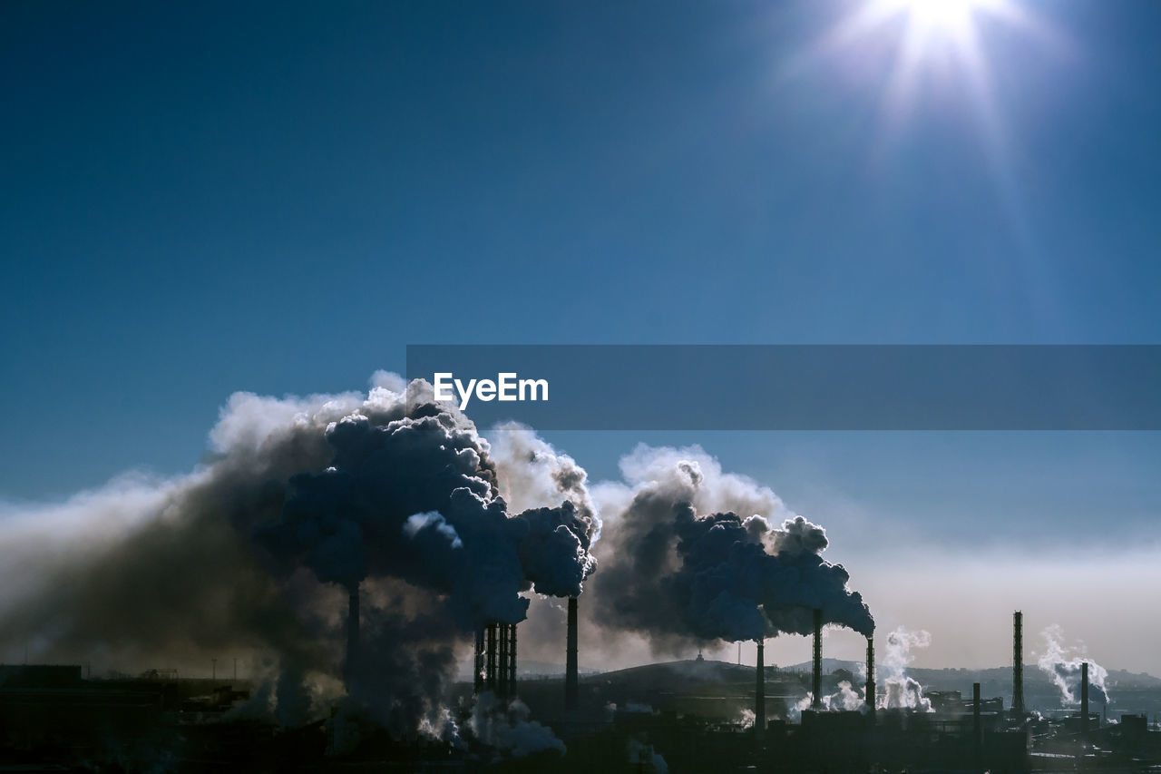 Smoke emitting from factory against sky on sunny day