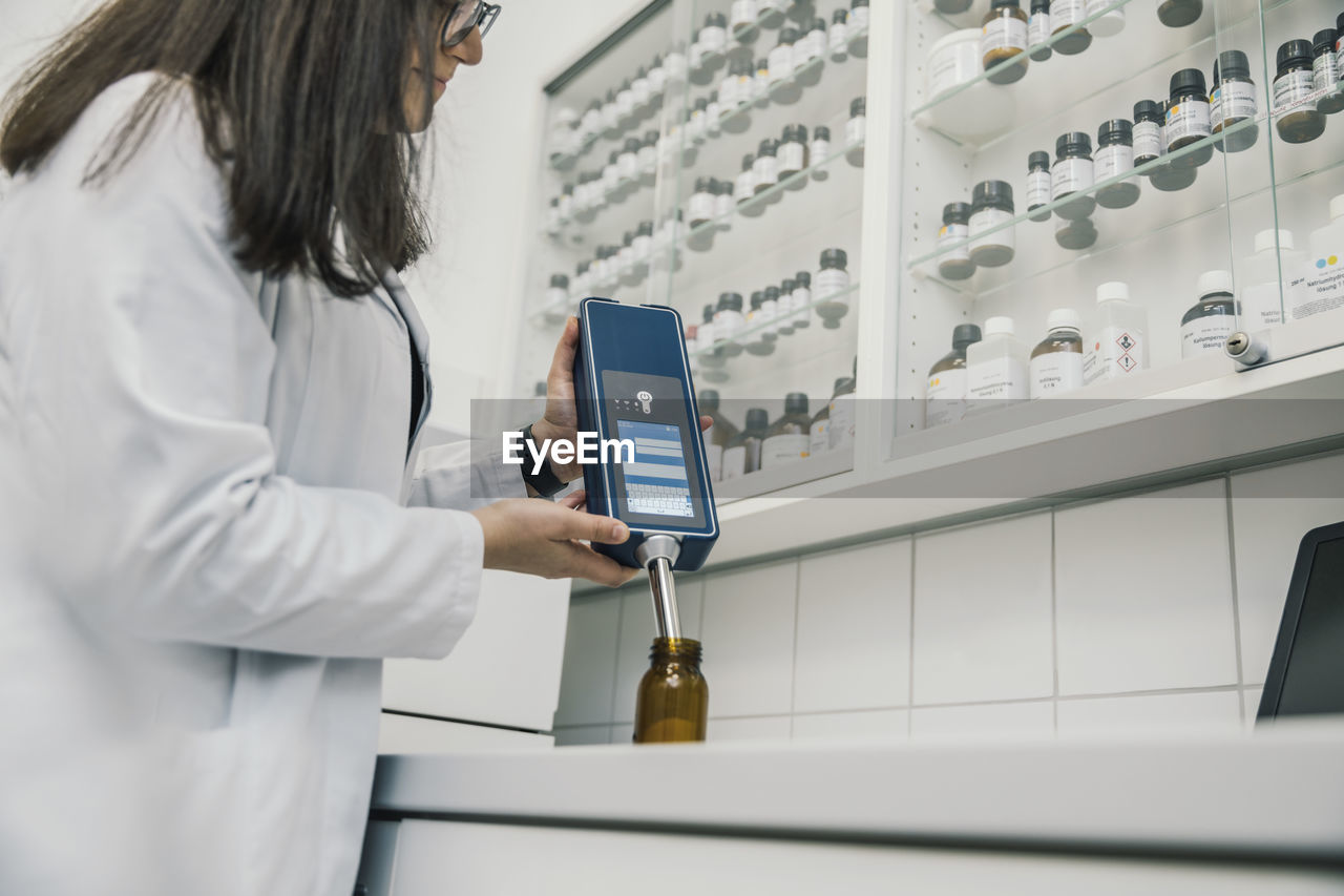 Midsection of female pharmacist using nir spectrometer in chemist store