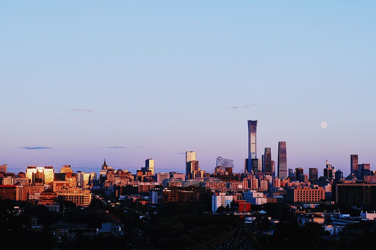 Buildings in city against clear sky during sunset