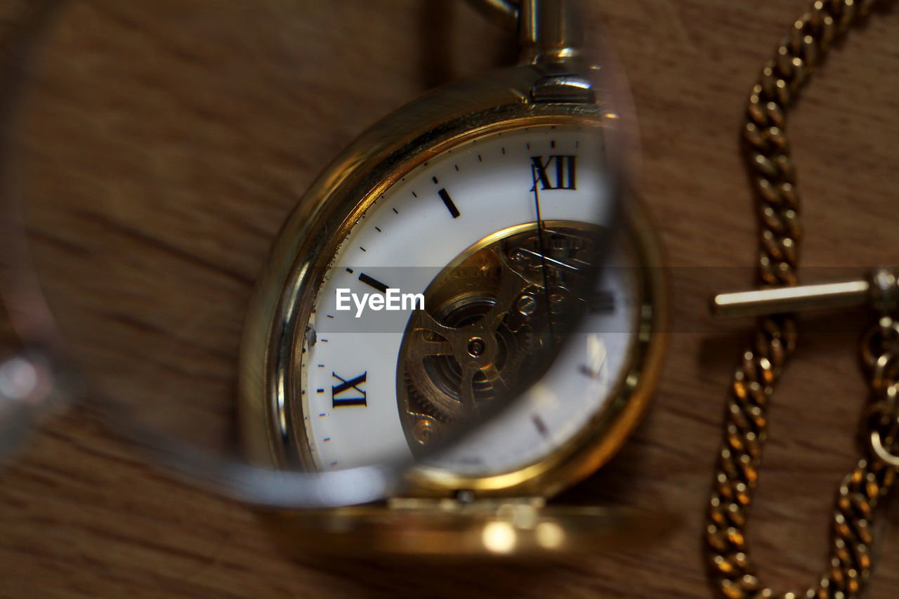 Close-up of magnifying glass over pocket watch on table
