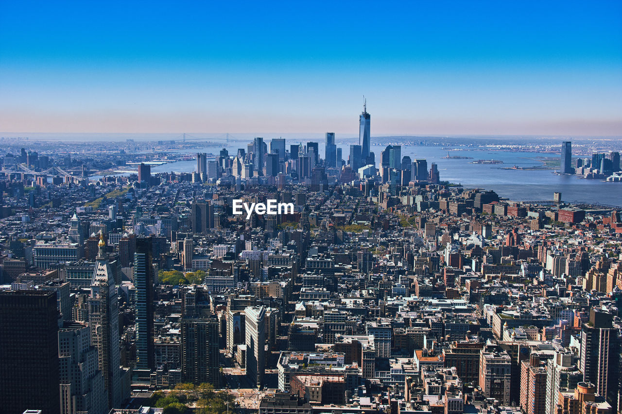 Modern cityscape by sea against clear blue sky