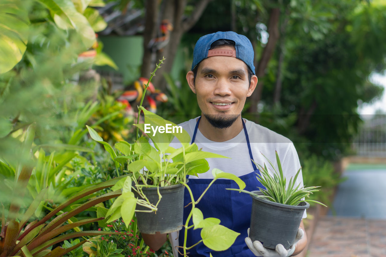 PORTRAIT OF YOUNG MAN STANDING AGAINST PLANTS