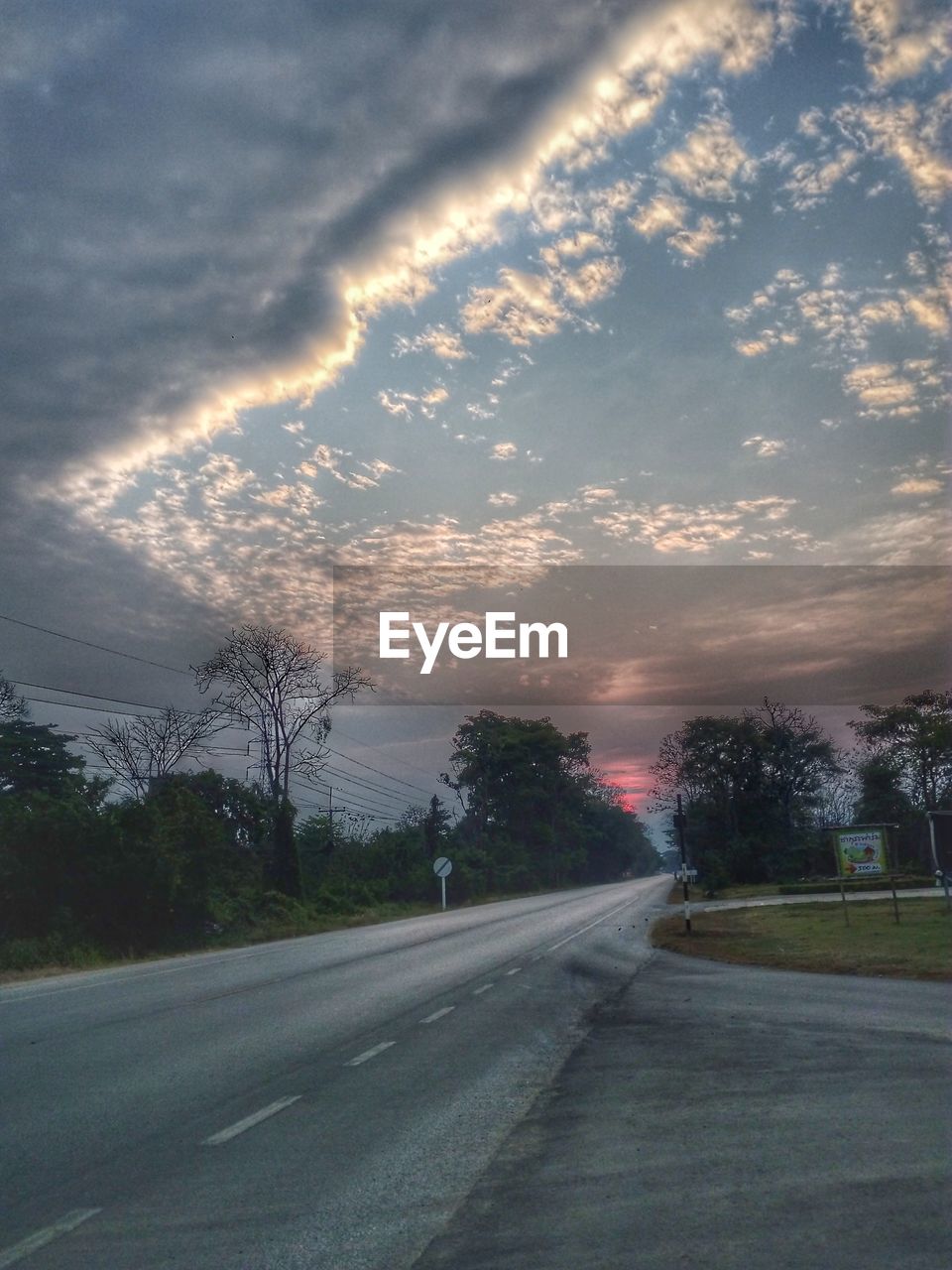 Road by trees against sky during sunset