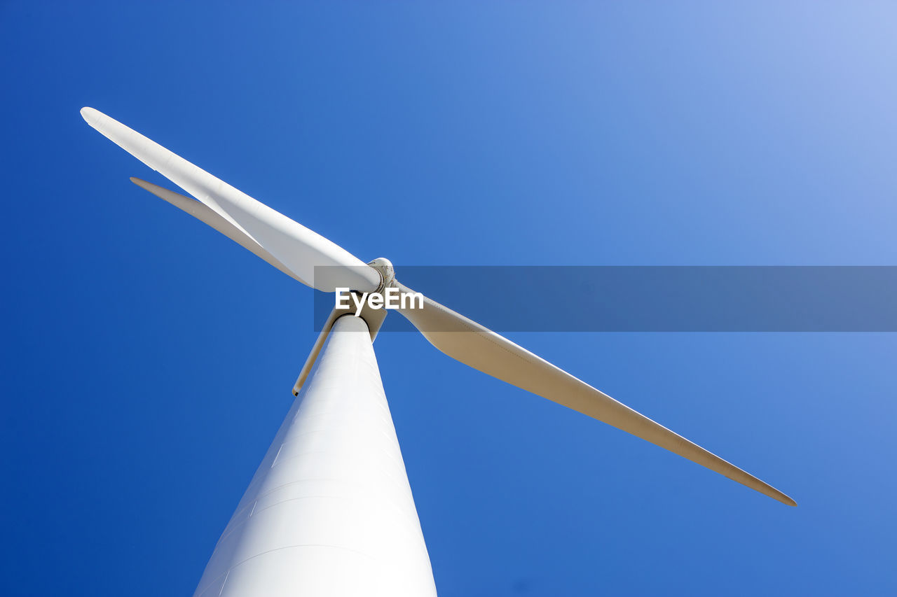 Looking up at wind turbine against blue sky