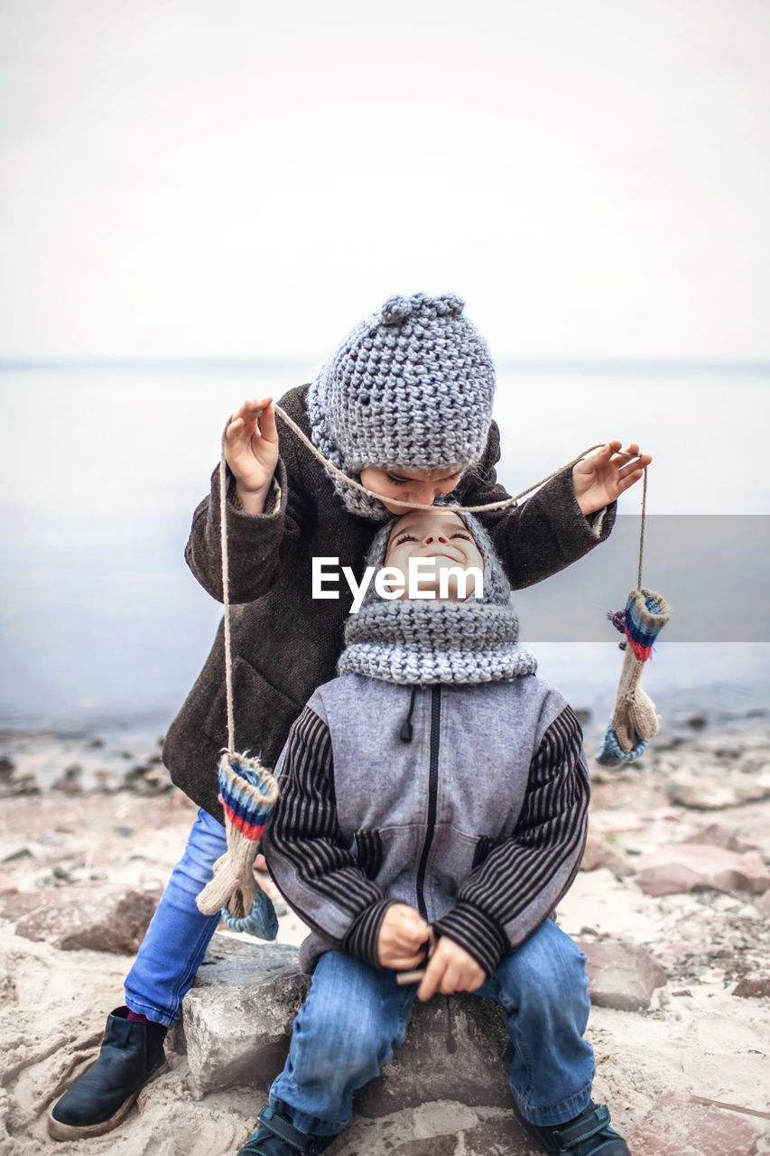 Girl in knitted grey hat sharing gloves with her frozen brother