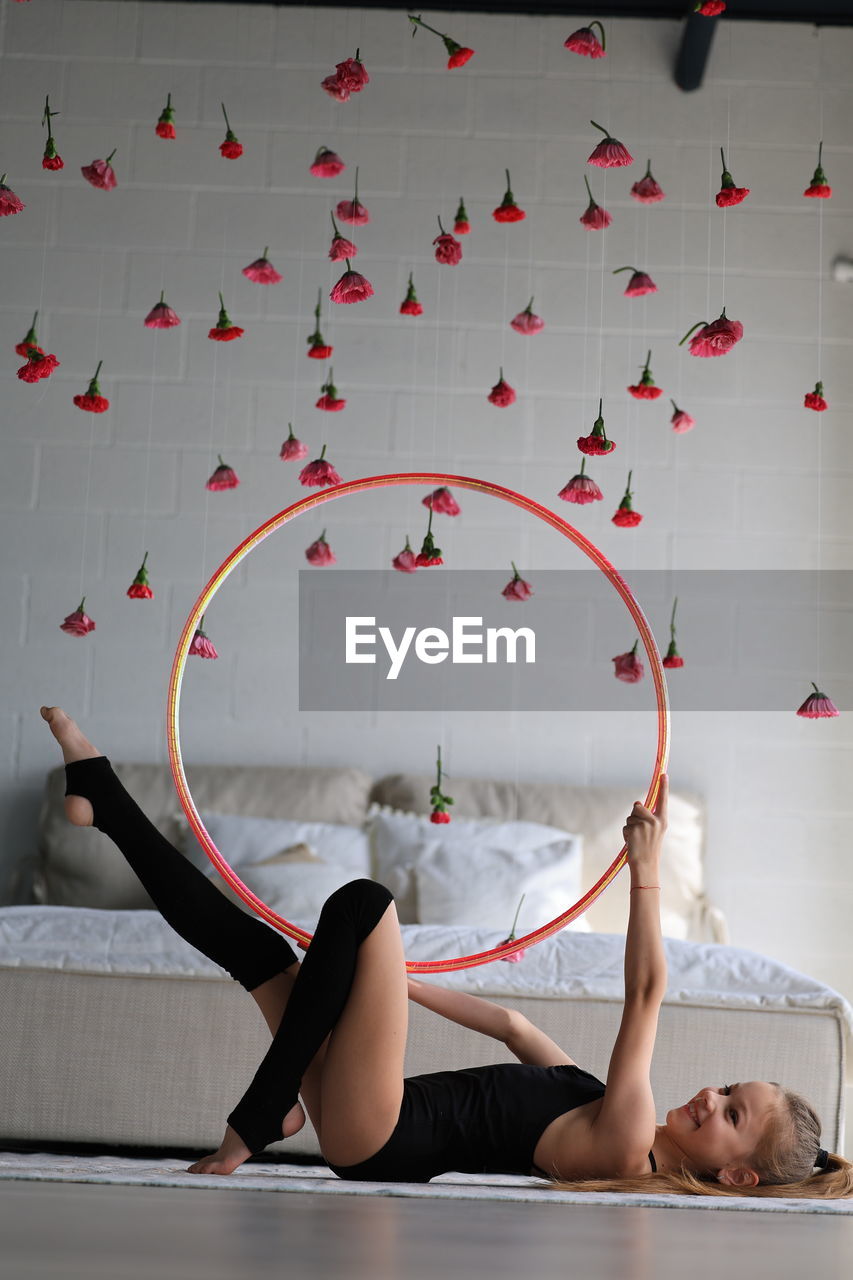 Little girl in sporty black clothes and leggings doing exercise with hoop on floor