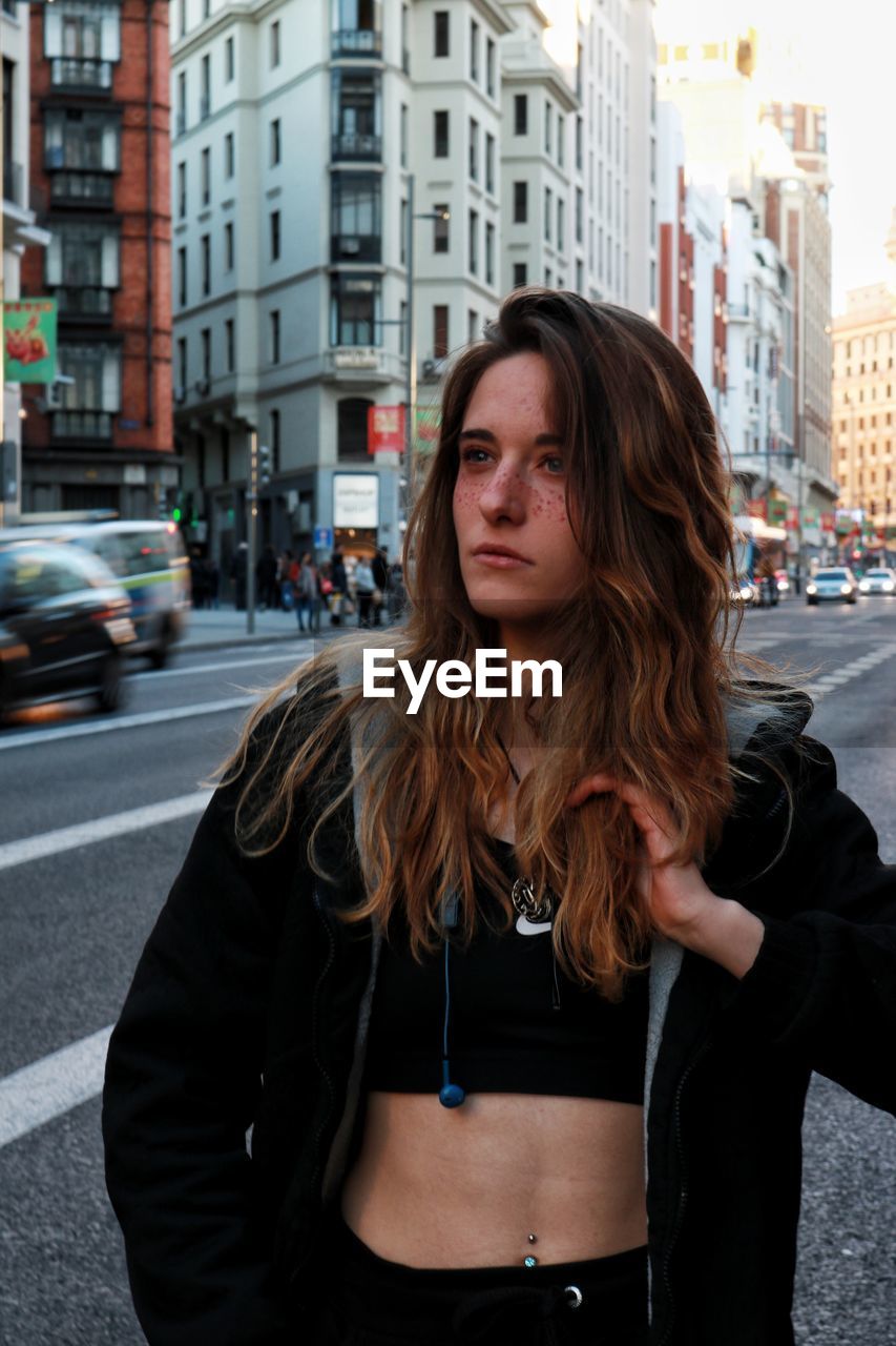 Beautiful young woman looking away while standing on street in city