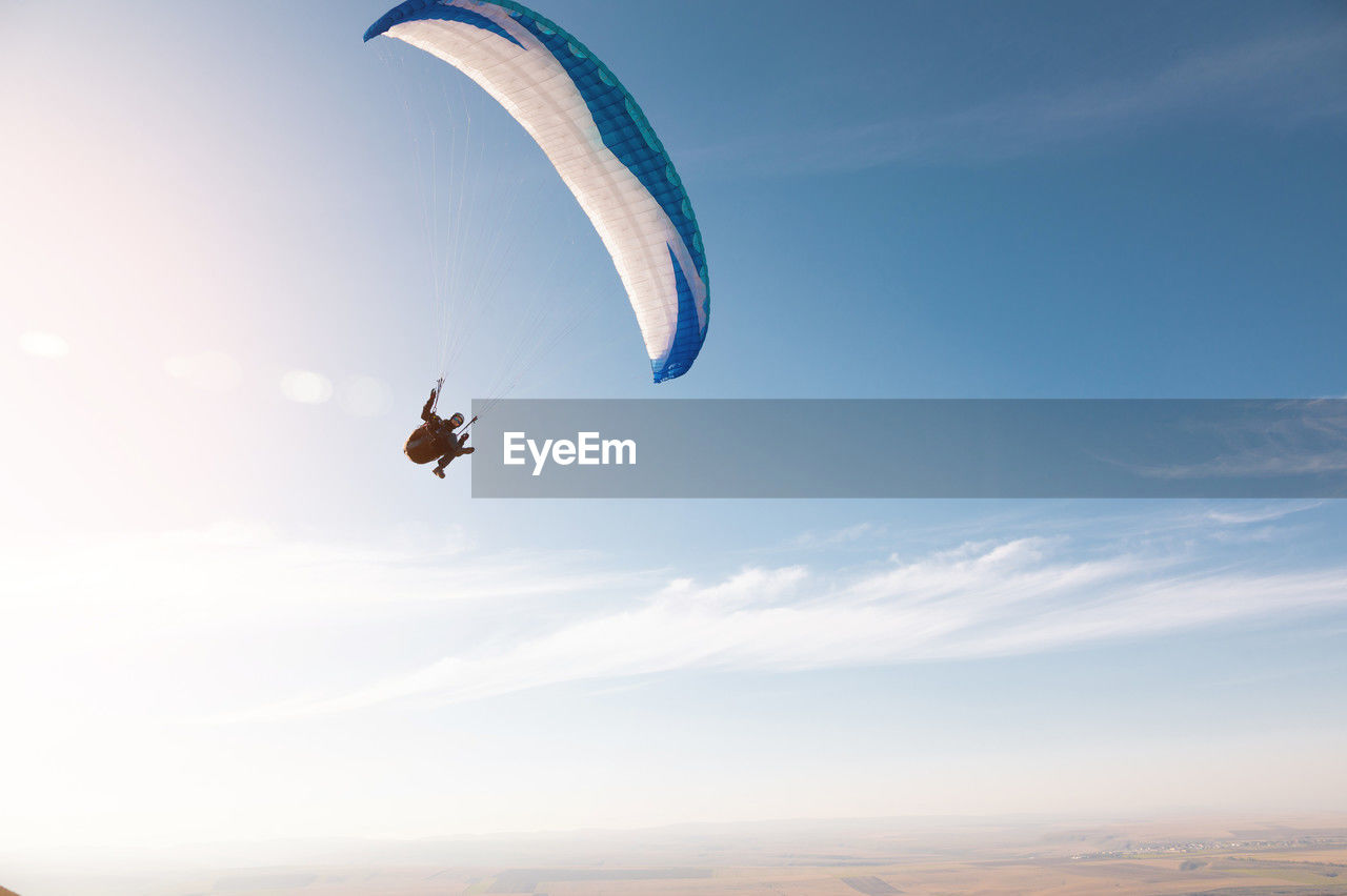 A paraglider with a blue parachute fly. a male flyght on the sky and lifts a paraglider into the air