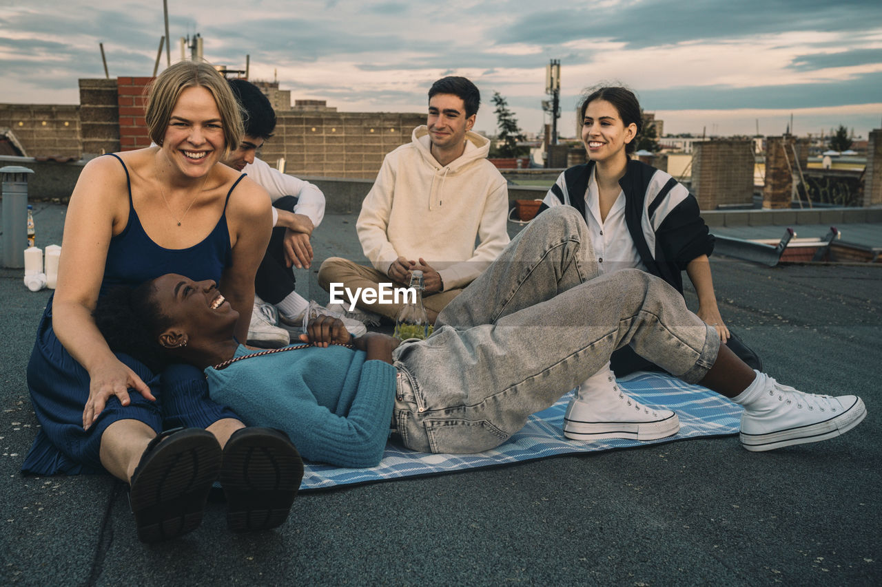 Cheerful male and female friends enjoying on building terrace during sunset