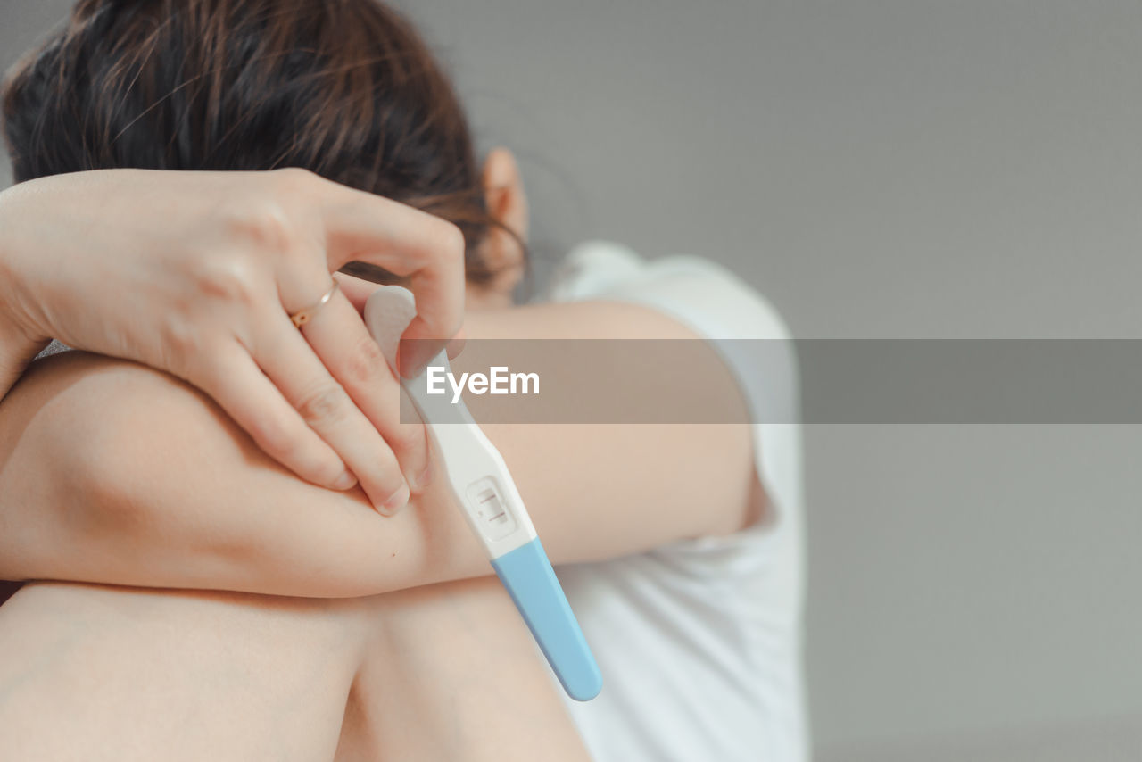 Close-up of woman holding pregnancy test strip on bed