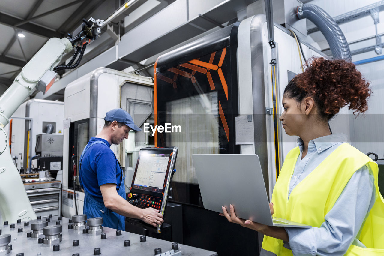 Engineer holding laptop and standing by colleague in industry