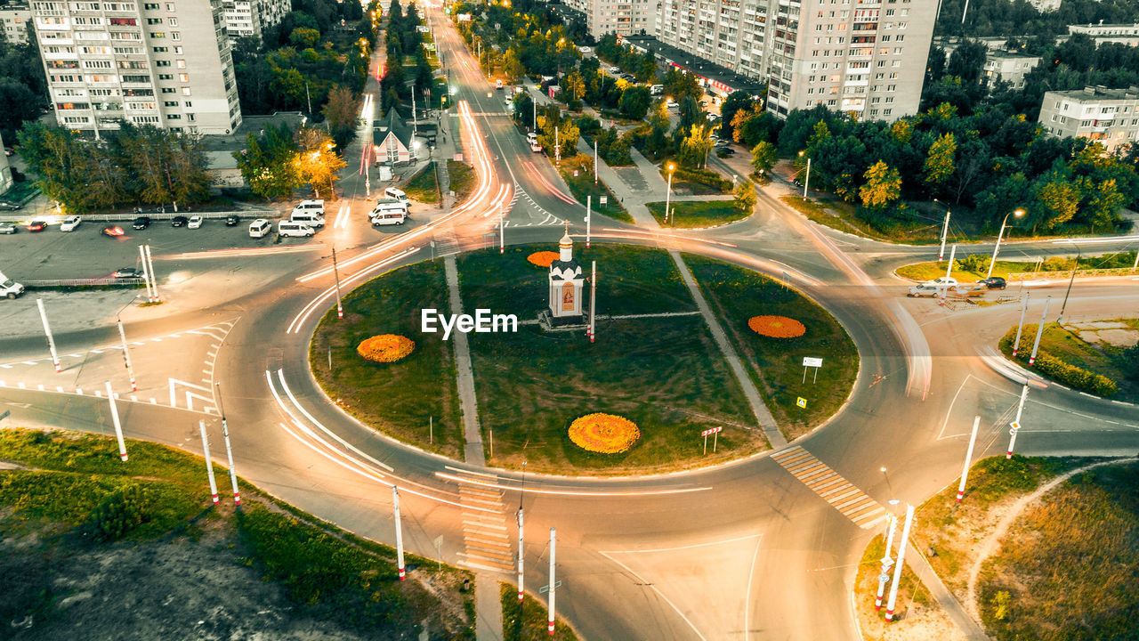 city, road, architecture, transportation, built structure, street, building exterior, metropolitan area, traffic, high angle view, intersection, mode of transportation, junction, motor vehicle, car, aerial photography, highway, city street, plant, infrastructure, urban area, nature, tree, cityscape, building, motion, city life, land vehicle, traffic circle, aerial view, landmark, symbol, no people, travel, sign, speed, outdoors, neighbourhood, lane, travel destinations, curve, light trail, residential district, crossroad, long exposure, residential area, illuminated, urban design, metropolis, landscape, bird's-eye view, sports, night, road intersection, town square, multiple lane highway, tail light