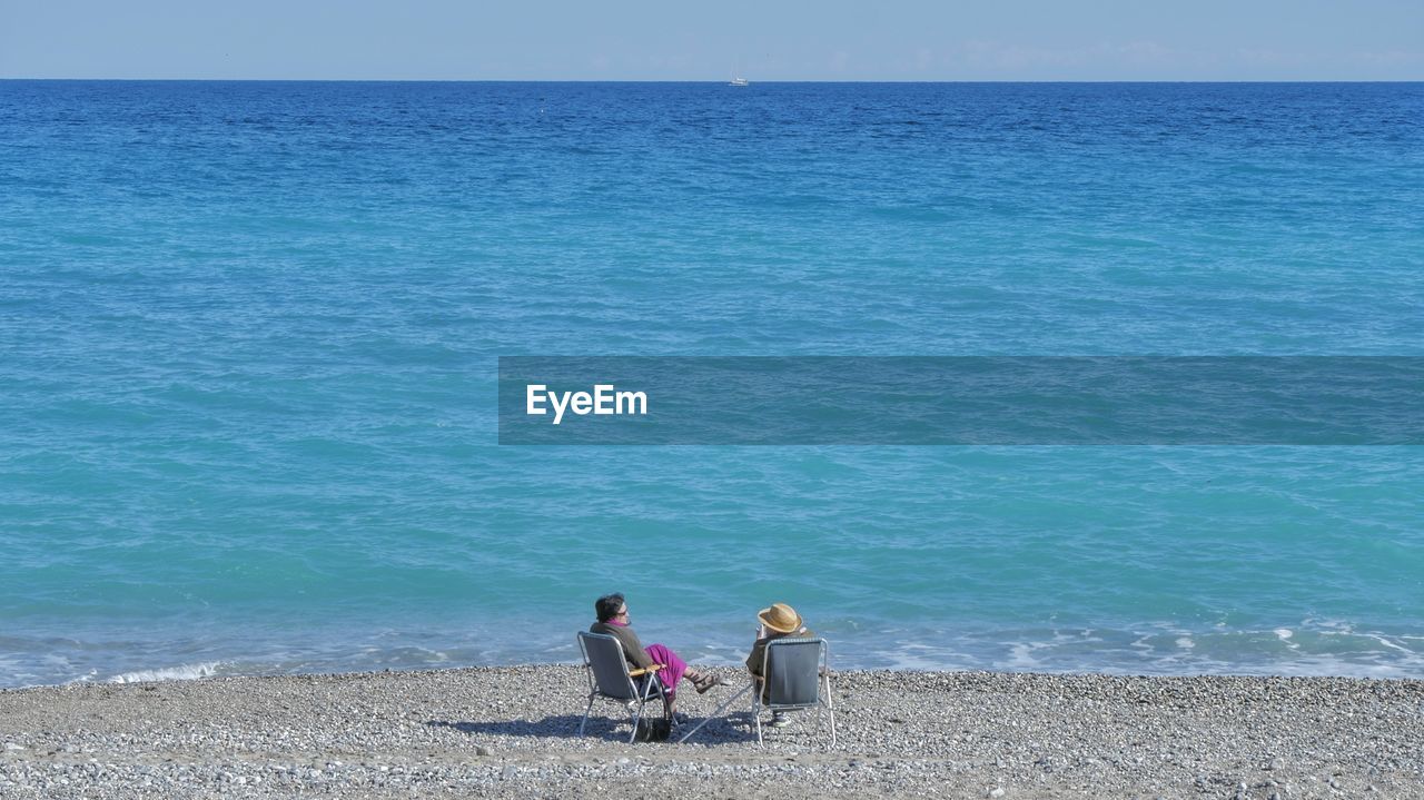 REAR VIEW OF PEOPLE ON BEACH AGAINST SKY