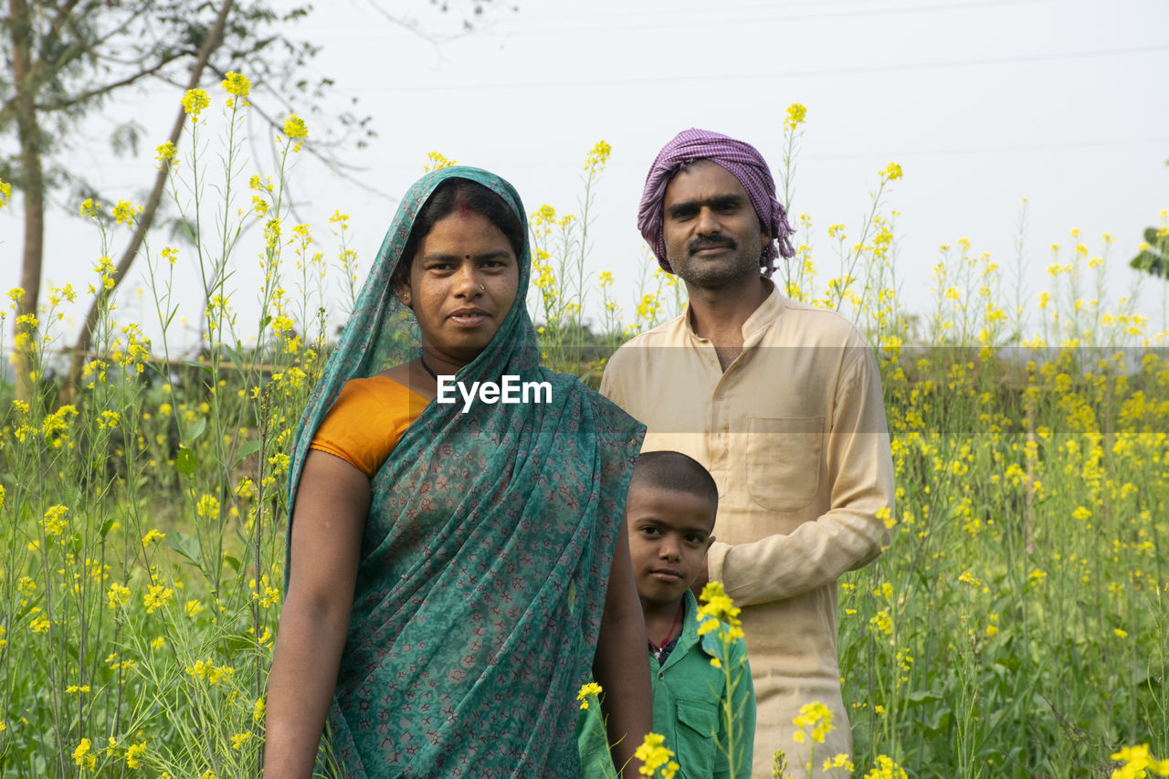 YOUNG COUPLE STANDING ON FIELD AGAINST YELLOW AND PLANTS